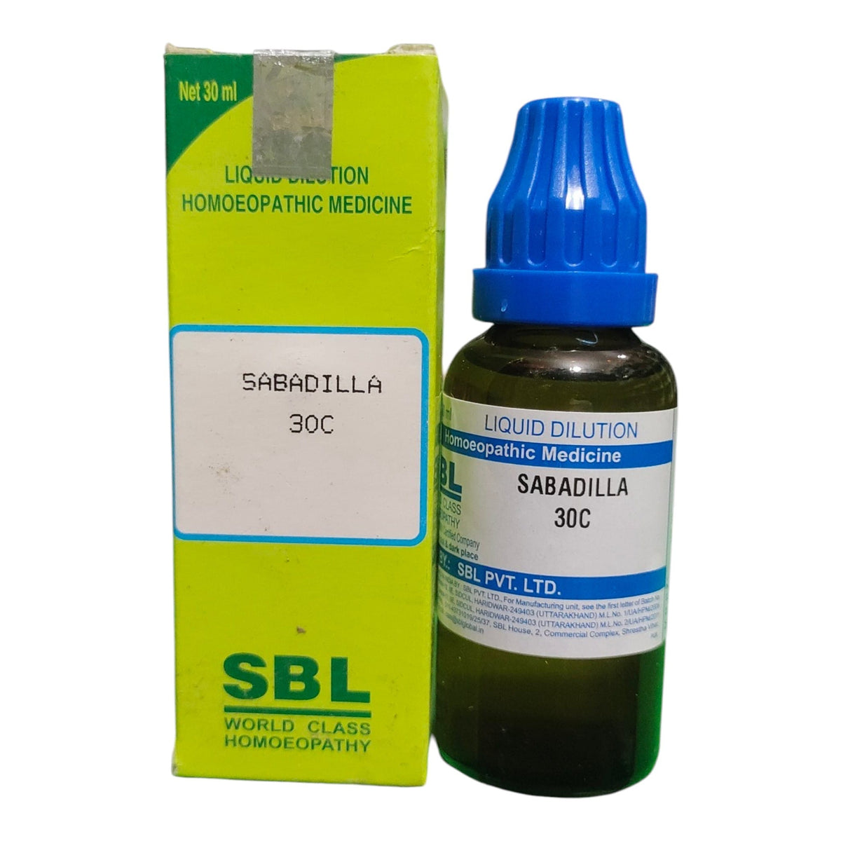 A bottle of SBL Sabadilla 30C homeopathic liquid medicine next to its lime green box packaging, on a plain white background.